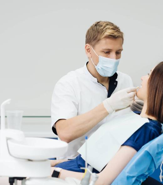 Close up portrait of beautiful young lady sitting in dental chair while stomatologist hands in sterile gloves holding tooth samples. She is smiling